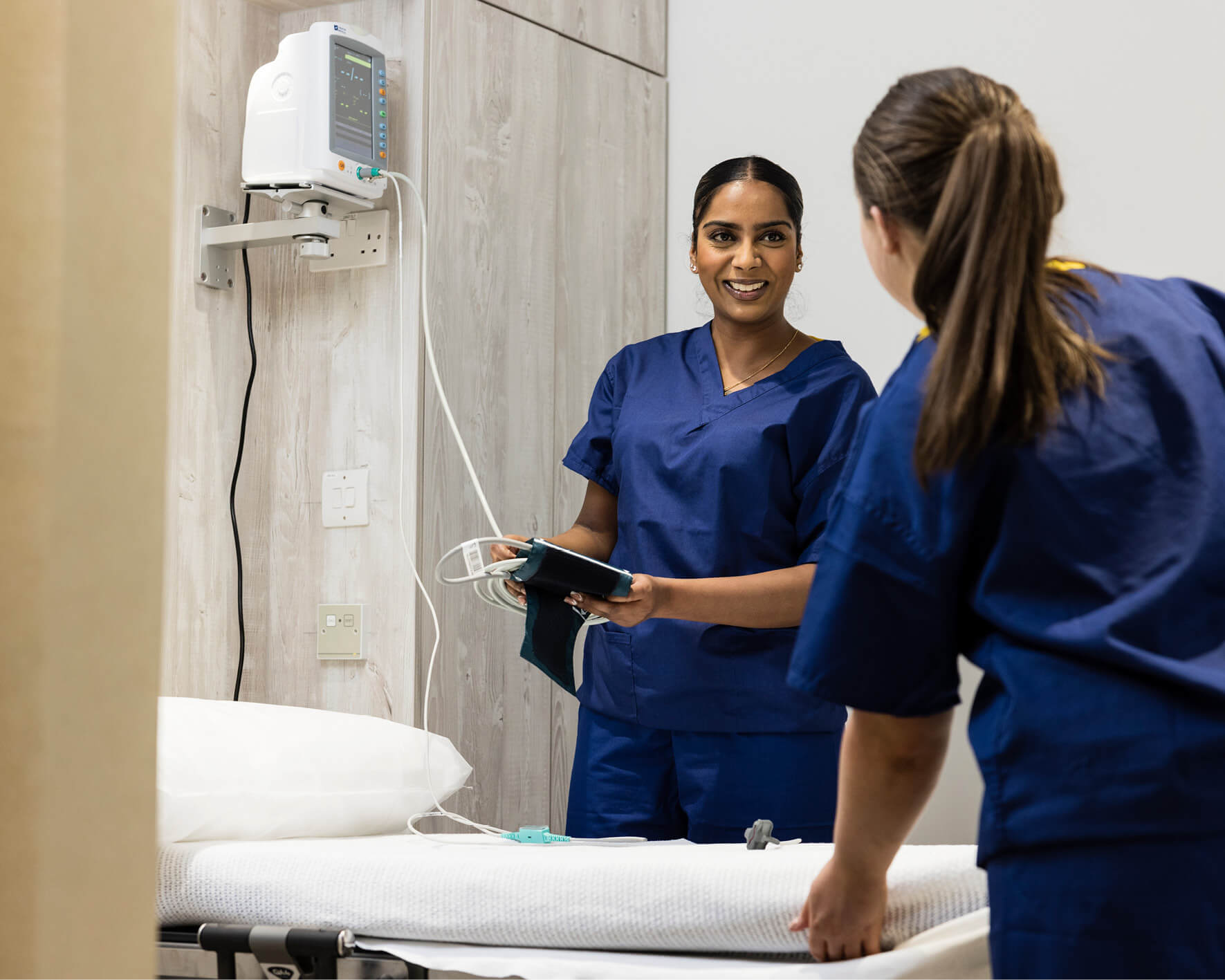 Two female fertility nurses wearing scrubs, chatting to eachother and setting up a patient's room for her fertility treatment