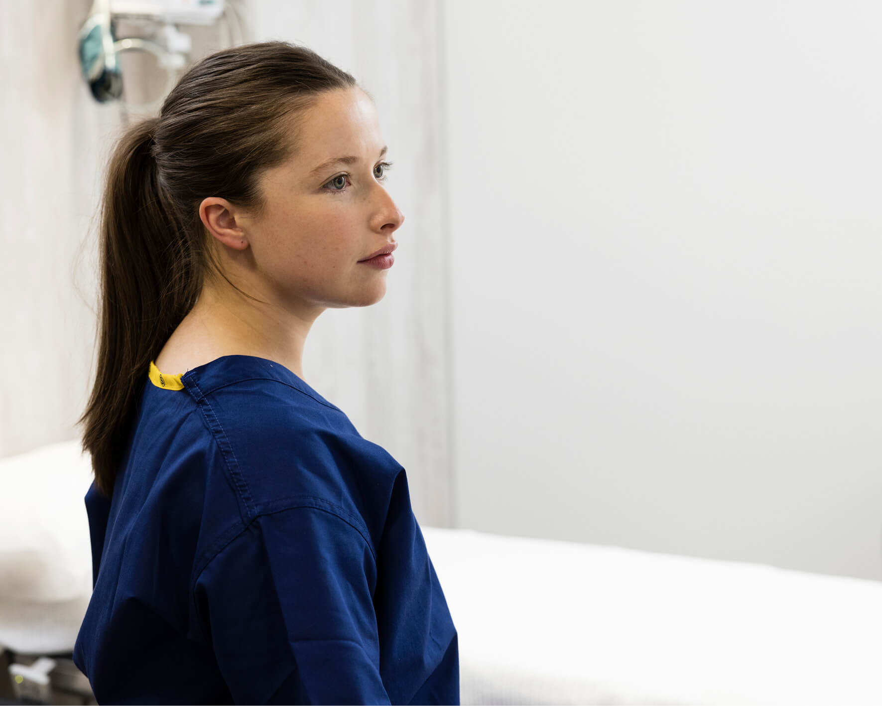 Fertility nurse in scrubs, standing in a treatment room looking into the distance